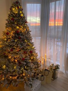 a white christmas tree with red and gold ornaments in front of a window at sunset