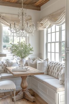 a room with white furniture and a chandelier hanging from the ceiling over a wooden table