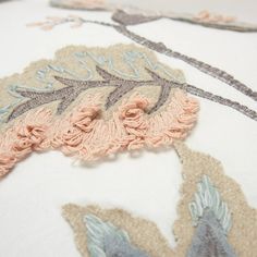 an embroidered piece of fabric on top of a white pillow with pink and blue flowers