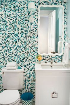 a white toilet sitting under a bathroom mirror next to a blue and white wallpaper