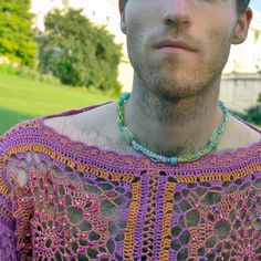 a man wearing a purple and orange crochet shirt in front of a building