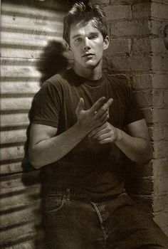 a young man sitting against a brick wall with his hands folded in front of him