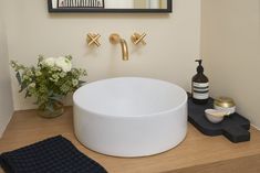 a white sink sitting on top of a wooden counter next to a vase with flowers