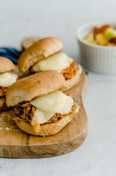 three sandwiches with meat and cheese on a cutting board