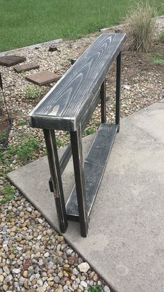 a wooden bench sitting on top of a cement slab next to gravel and grass covered ground