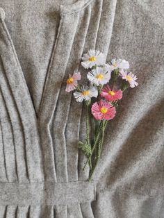 a bunch of flowers that are in the pocket of a gray sweater dress on a table