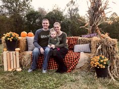 a man, woman and child sitting on a hay bale with pumpkins in the background