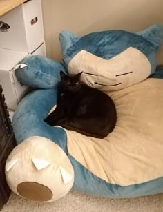 a black cat laying on top of a blue and white stuffed animal bed next to a dresser