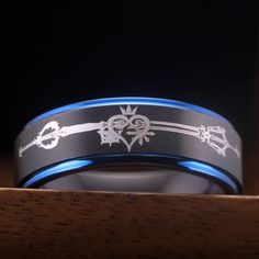 two wedding bands with an arrow and heart design are shown on a wooden surface in front of a black background