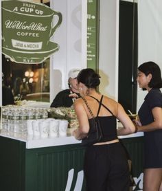 two women standing at a counter in front of a coffee shop with cups on it