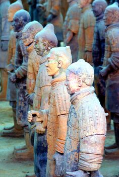 some very old statues that are standing in a row together on the ground, and one is pointing at something