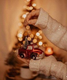 a person holding a christmas ornament in front of a small tree with lights