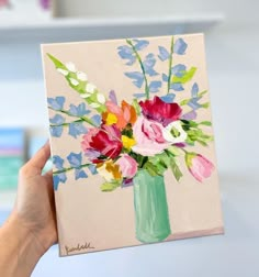 a painting of flowers in a vase is being held up by a woman's hand