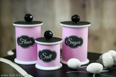 three pink canisters with black labels on them and white balls in the middle