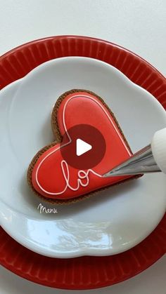 a person cutting into a heart shaped cookie on top of a white and red plate