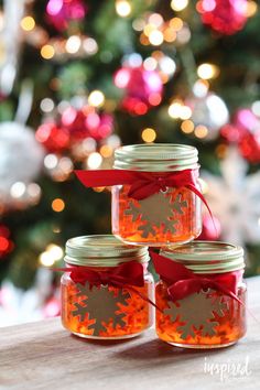 three glass jars with red ribbon and snowflakes are sitting on a table in front of a christmas tree