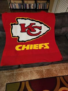 a blanket with the kansas chiefs logo on it is sitting on a couch in front of a bookcase