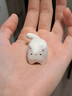 a small white cat figurine sitting on the palm of someone's hand