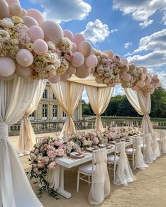 an outdoor wedding setup with pink and white flowers on the table, balloons in the air