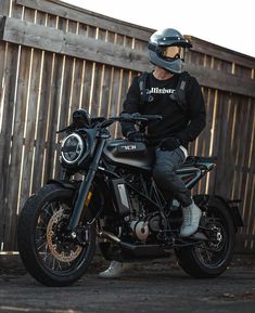 a man sitting on top of a motorcycle next to a wooden fence and wearing a helmet