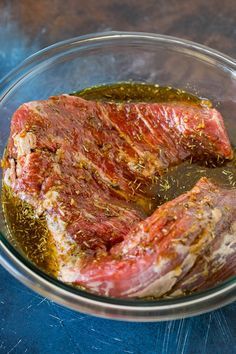 raw meat in a glass bowl on a blue counter top, with seasoning sprinkles