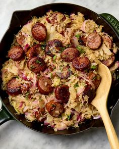 a skillet filled with sausage and sauerkraut next to a wooden spoon