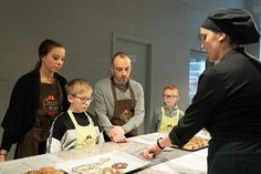 a group of people standing around a table with food on it and one person wearing an apron