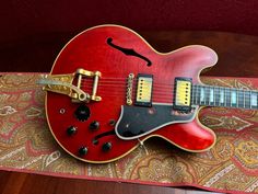 a red electric guitar sitting on top of a wooden table next to a paisley rug