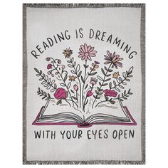 an open book with flowers and the words reading is dreaming, with your eyes open