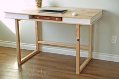 a wooden desk with a laptop on top and a vase sitting next to it in front of a wall