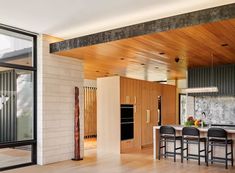 an open kitchen and dining room area with wood flooring, white counter tops and black bar stools