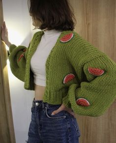 a woman is wearing a green sweater with watermelon patches on it and has her hands in her pockets