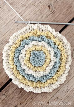 a crocheted dishcloth on a wooden surface with knitting needles in the background