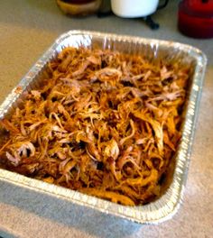 a metal pan filled with shredded meat on top of a counter next to a cup