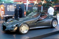 a silver sports car on display in a showroom with people looking at the cars