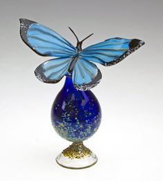 a glass butterfly sitting on top of a blue vase