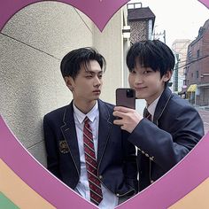 two young men taking a selfie in front of a heart - shaped photo frame