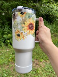 a hand holding a white coffee cup with sunflowers painted on the bottom and sides