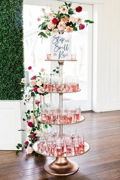 a tiered cake with wine glasses and flowers on the top is surrounded by greenery