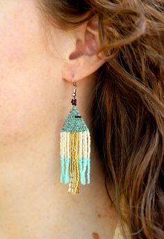 Handmade by fair trade artisans in Tanzania, these shimmery beaded triangle earrings are full of texture and life! Lightweight and easy to wear, these gorgeous earrings support the livelihood of women artisans, all with flawless style. Features include: Beaded by hand in Mbeya, Tanzania Multifaceted turquoise, cream, gold, and light blue Miyuki glass beads Hypoallergenic sterling silver ear wire Created by 4 different beading cooperatives, which together support over 40 female artisans A portion Bohemian Triangle Beaded Earrings, Blue Bohemian Triangle Earrings, Bohemian Blue Triangle Earrings, Bohemian Triangle Jewelry With Dangling Beads, Mbeya Tanzania, Gold And Light Blue, Aids Hiv, Triangle Earrings, Women Artisans