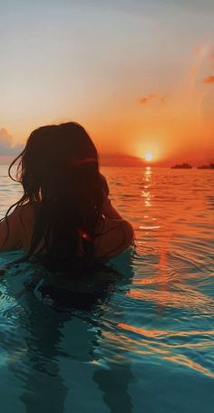 a woman sitting in the water at sunset with her back to the camera and arms behind her head