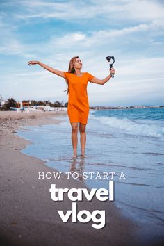 a woman in an orange dress is standing on the beach with her arms spread out