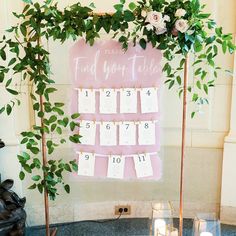 a pink and white wedding seating chart with greenery on the top, next to candles