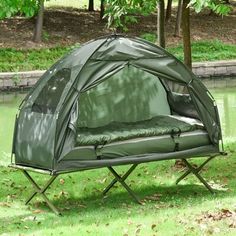 a green tent sitting on top of a lush green field next to a lake with trees in the background