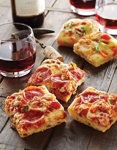 several slices of pizza sitting on top of a wooden table next to glasses of wine