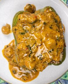 a white plate topped with meat covered in gravy next to green peppers and sauce