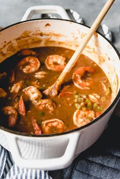 a pot filled with shrimp and vegetables on top of a blue striped cloth next to a wooden spoon