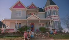 two people sit on the steps in front of a house with pink trim and white windows