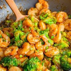 broccoli and shrimp are being cooked in a wok with a wooden spoon