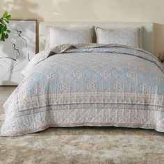 a bed with a blue and white comforter on top of it next to a potted plant